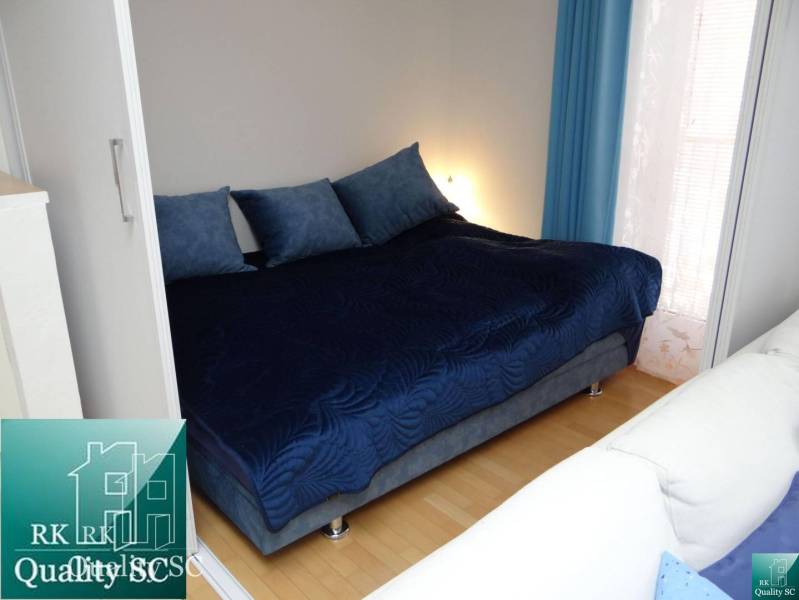 A bedroom in a one-room apartment with a large bed and a floor with a wooden decor.