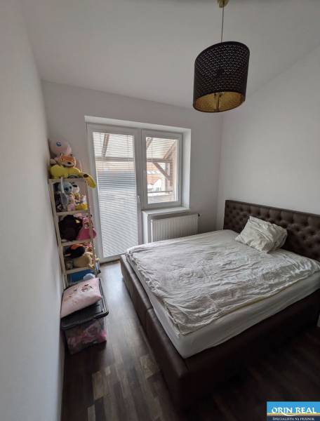 Bedroom in a 2-room apartment with a bed, shelf, and wooden decor flooring.