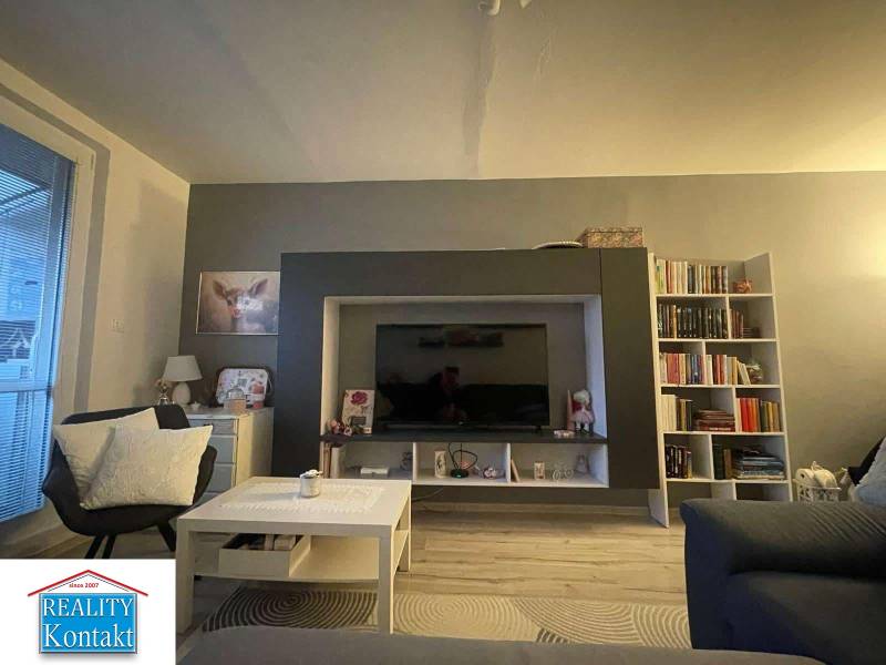 Living room with a sofa, television, bookshelf, and wooden decor flooring in a two-room apartment.