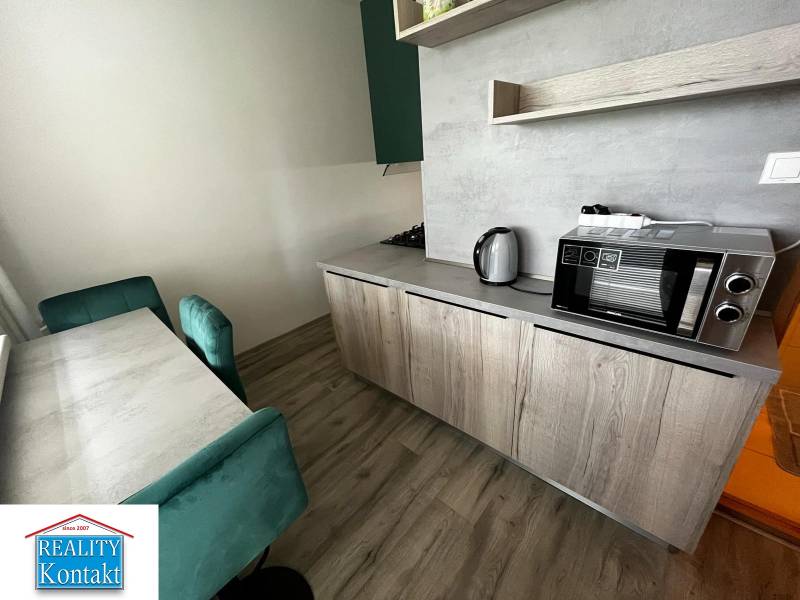 A kitchen in a 2-room apartment with a wooden decor floor, table, chairs, and appliances.