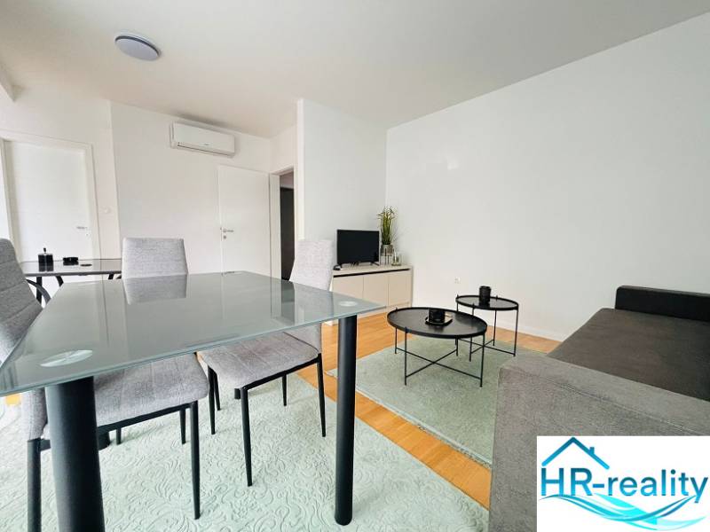 Living room with a sofa, folding table, and wood-patterned floor in a holiday apartment.