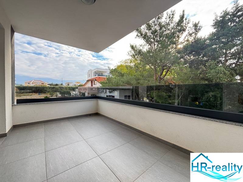 The terrace of a recreational apartment in Novalja with glass railings and a view of the surrounding houses.