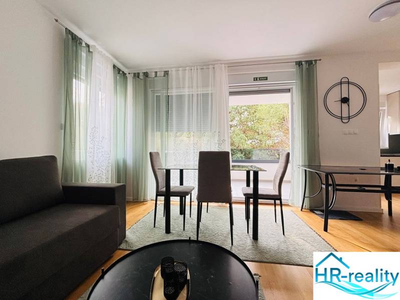 Living room of a holiday apartment with a sofa, dining table, and wood-patterned flooring.