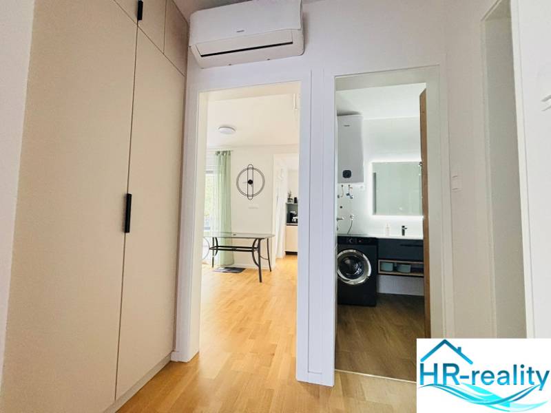 Hallway of a holiday apartment with a view of the bathroom and living room, floor with wooden decor.