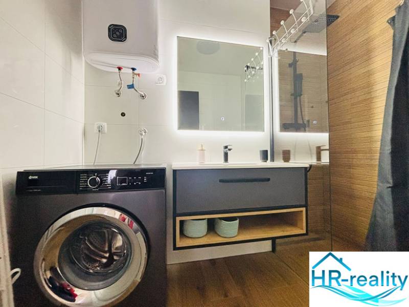 Bathroom with a washing machine, sink, mirror, and boiler. Floor with wood decor.
