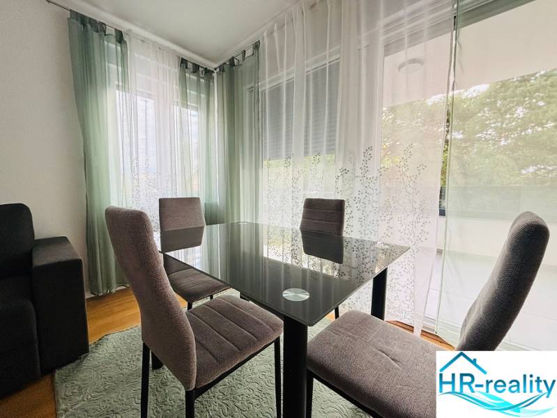 Dining area in a holiday apartment with wood-patterned flooring and sheer curtains.