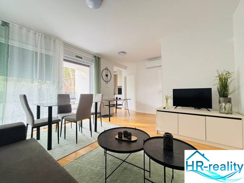 Recreational apartment with wood-patterned flooring, dining table, and television on a cabinet.