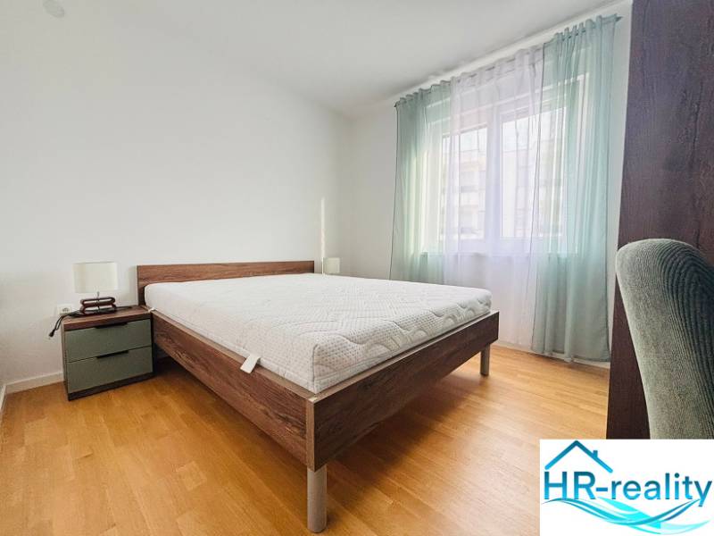 Recreational apartment with a bed, nightstand, light curtains, and a floor with a wooden decor.