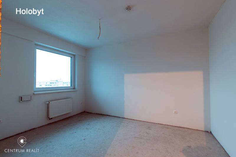 An empty room without flooring in a 2-room apartment with a large window and a radiator.