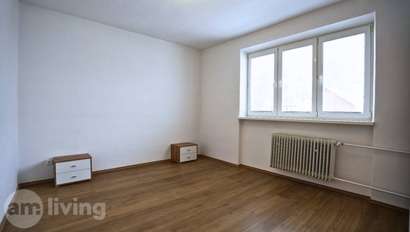 A room in a 3-room apartment with a wooden decor floor and simple furniture.