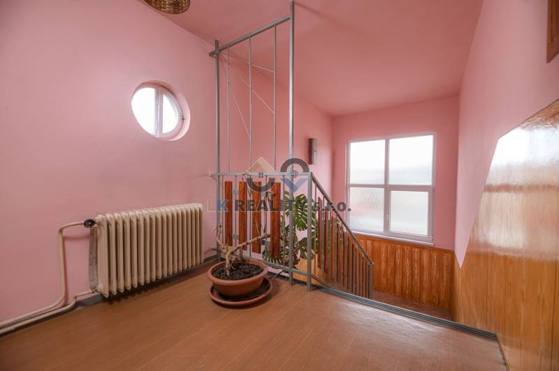 A staircase in a family house with a wooden decor, pink walls, and potted plants.