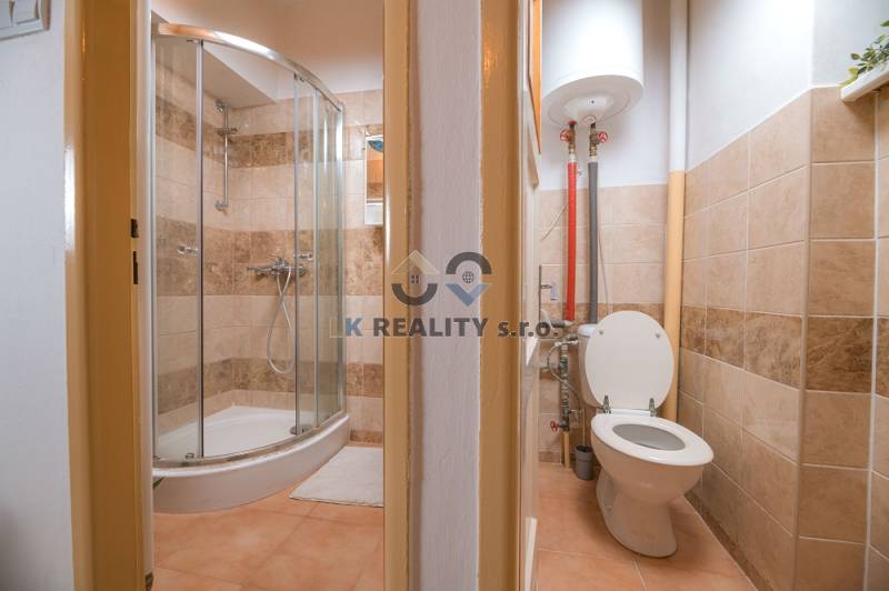 Bathroom in a family house with a corner shower and toilet, beige tiles.