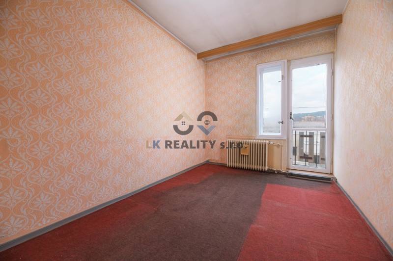 A room in a family house with a window, wallpaper, and a radiator, carpeted floor.