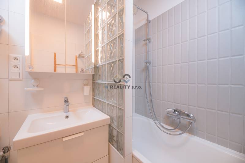 Bathroom in a 3-room apartment with a sink, mirror, and a bathtub with a glass wall.