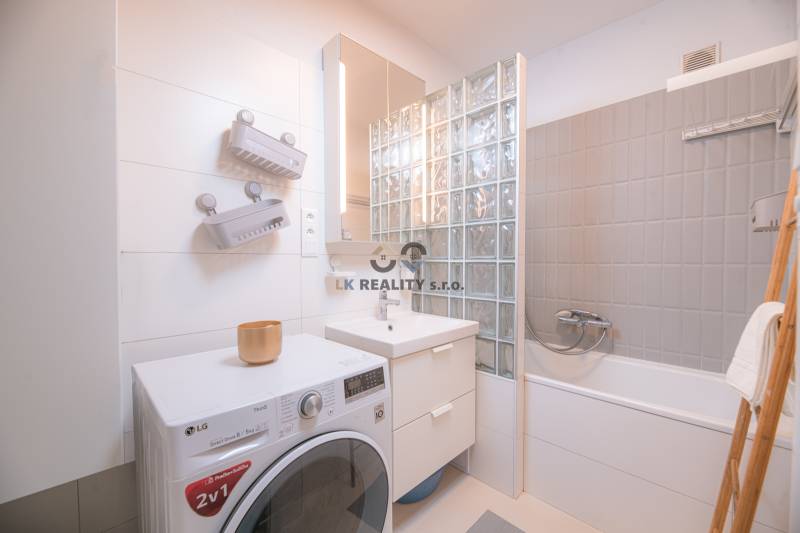 A bathroom in a 3-room apartment with a shower, a washing machine, and light tiles.