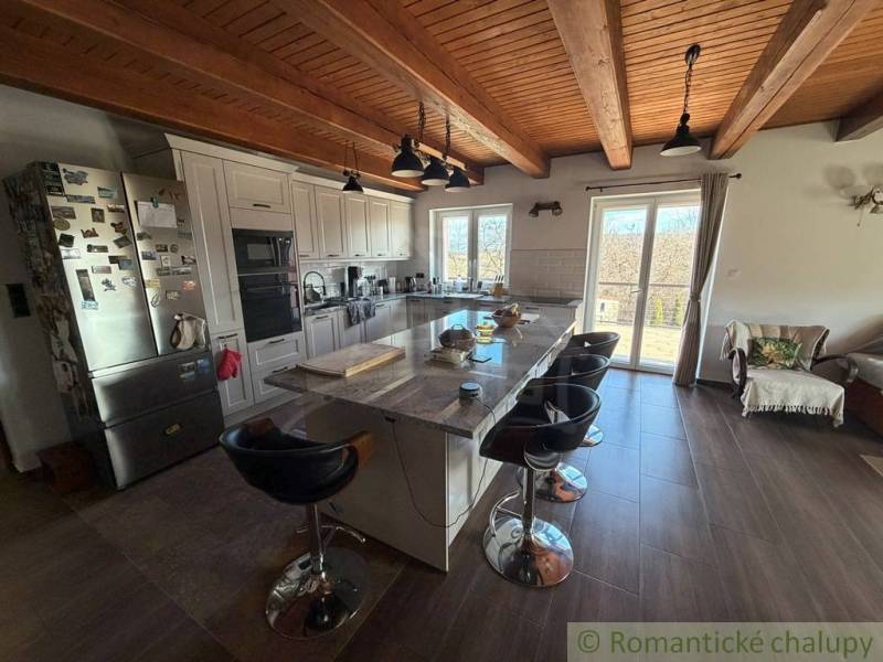 A kitchen in a family house with an island, a wooden decor floor, and a view outside.