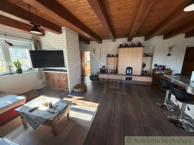 Living space with a wooden ceiling, wood-patterned floor, and a tiled stove in a family house.