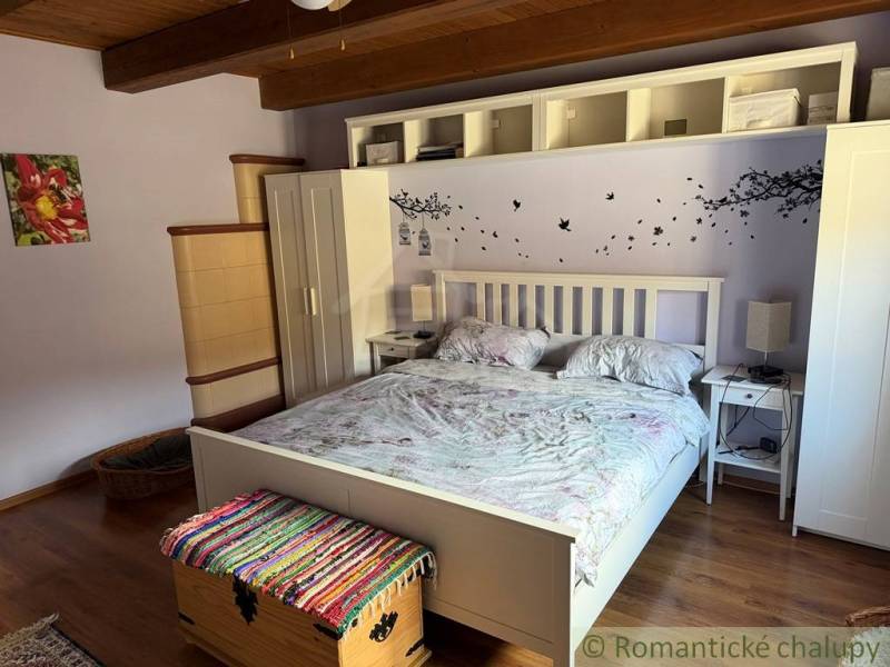 A bedroom in a family house with a bed, white furniture, and a wooden decor floor.