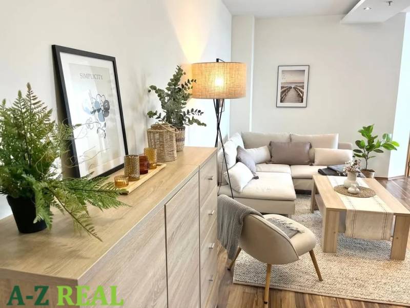 Living room in a three-room apartment furnished with light furniture and plants, with a wooden decor floor.