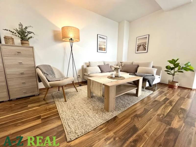 Living room in a three-room apartment with a wooden decor floor, light furniture, and a plant.