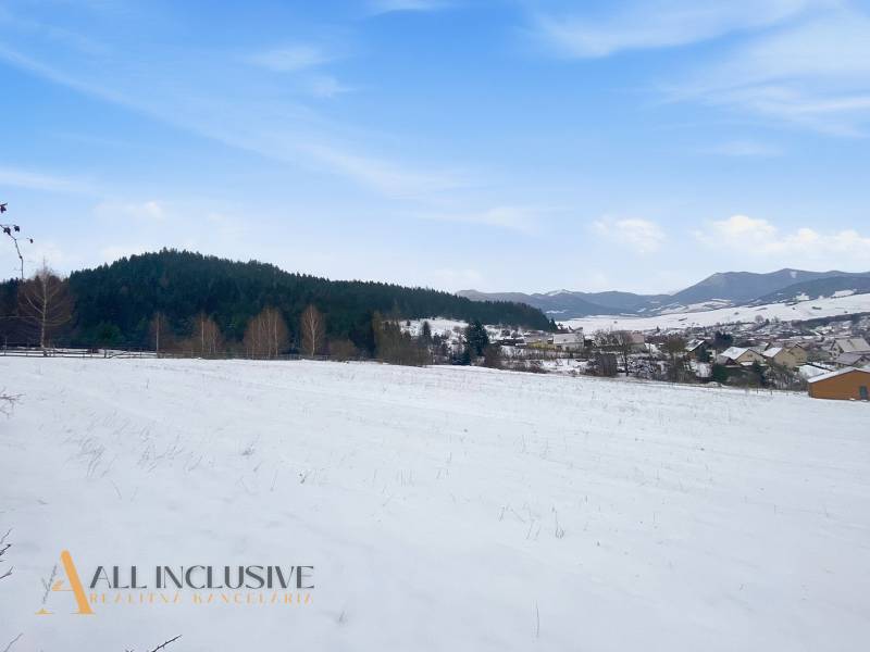 Snow-covered residential plots in Komjatná, surrounded by forests and mountains, with a view of the village.