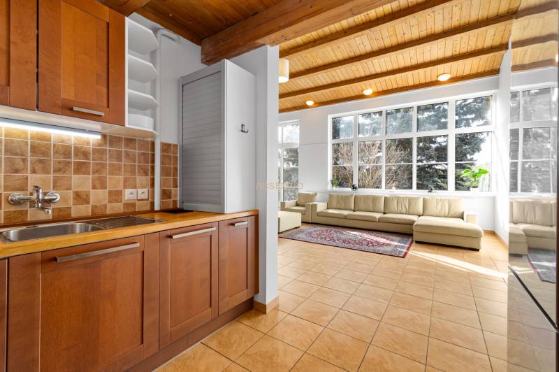 A kitchen with tiles and a wooden cabinet connected to the living room in a family house.
