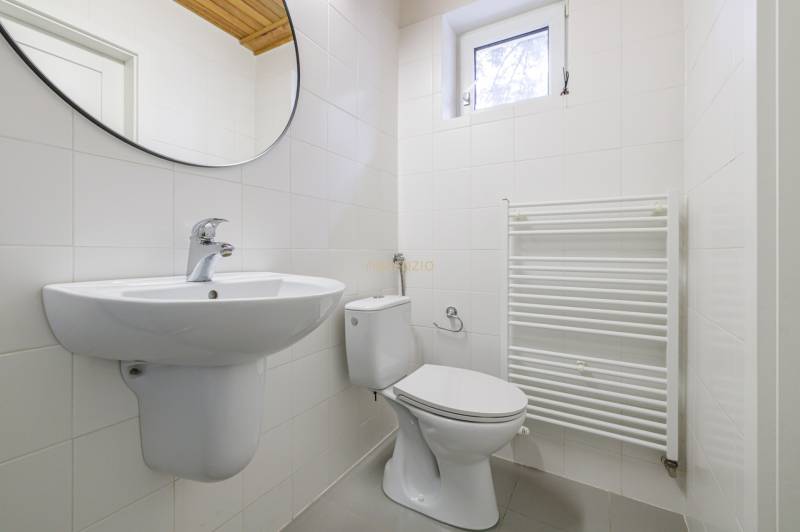 A bathroom in a family house with white tiles, a sink, a toilet, and a ladder radiator.