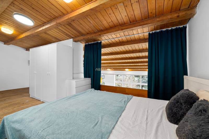 A bedroom in a family house with a wooden ceiling, a large window, and a floor with a wooden decor.