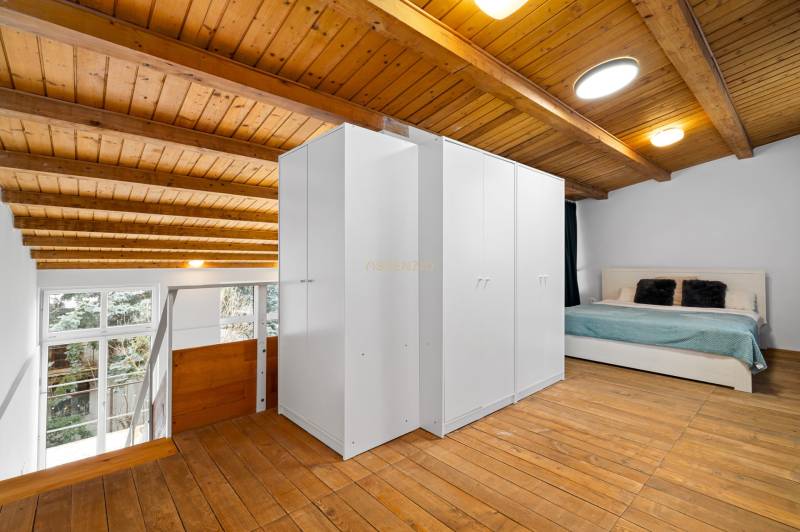 Attic bedroom in a family house with a wooden ceiling, floor with a wooden decor, and a bed.