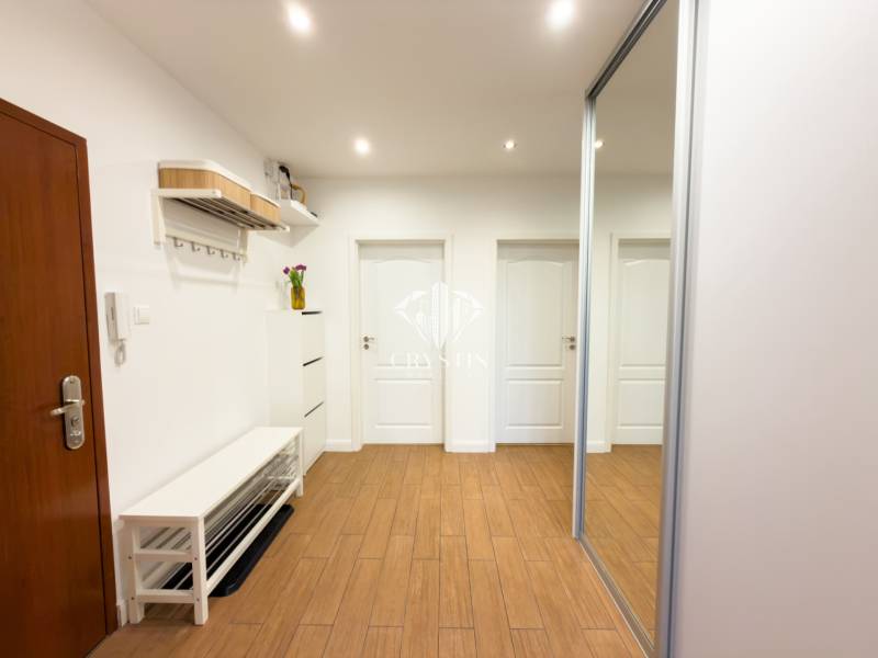 A hallway in a 4-room apartment with a wooden decor floor, a mirror, and coat racks.