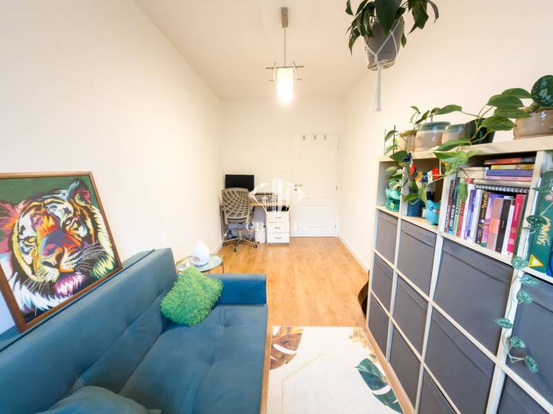 A room in a 4-room apartment with a sofa, a bookshelf, and a wooden decor floor.