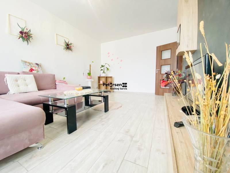 Living room in a three-room apartment with a wood-patterned floor and modern furniture.