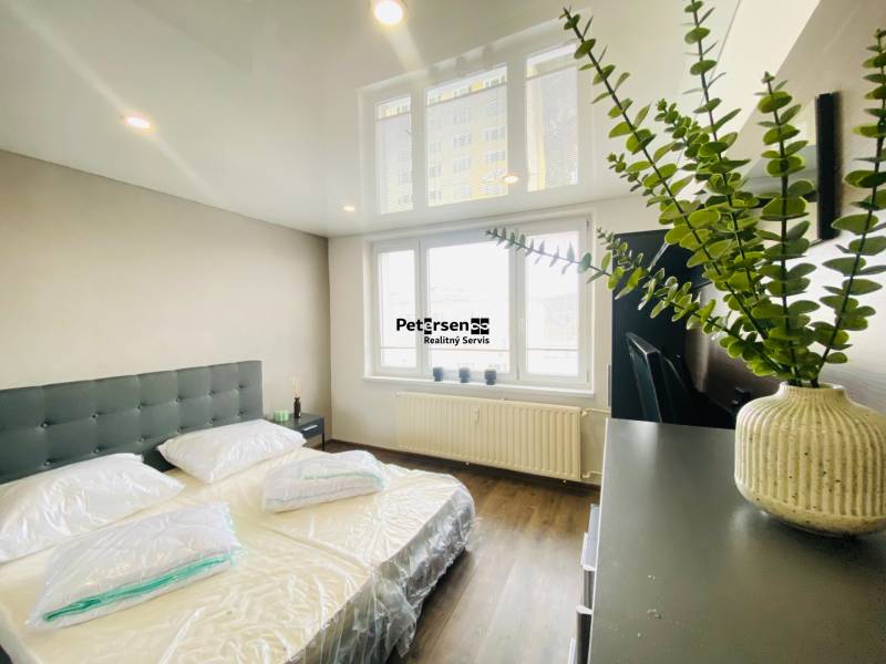 Bedroom in a three-room apartment with wood-patterned flooring and large windows.