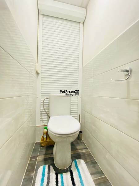 Bathroom in a 3-room apartment, white toilet, tiles, blind, shelf for products.