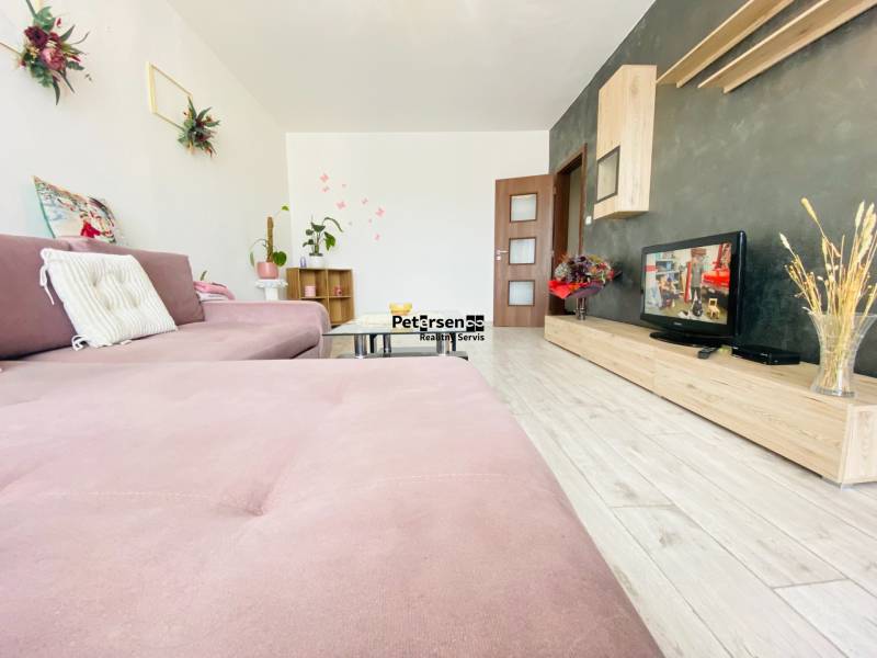 Living room in a 3-room apartment with a pink sofa, decorations, and a wooden-patterned floor.