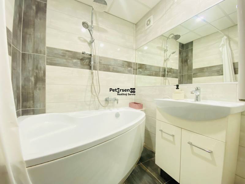 A bathroom in a 3-room apartment with a bathtub, sink, and tiles in light tones.