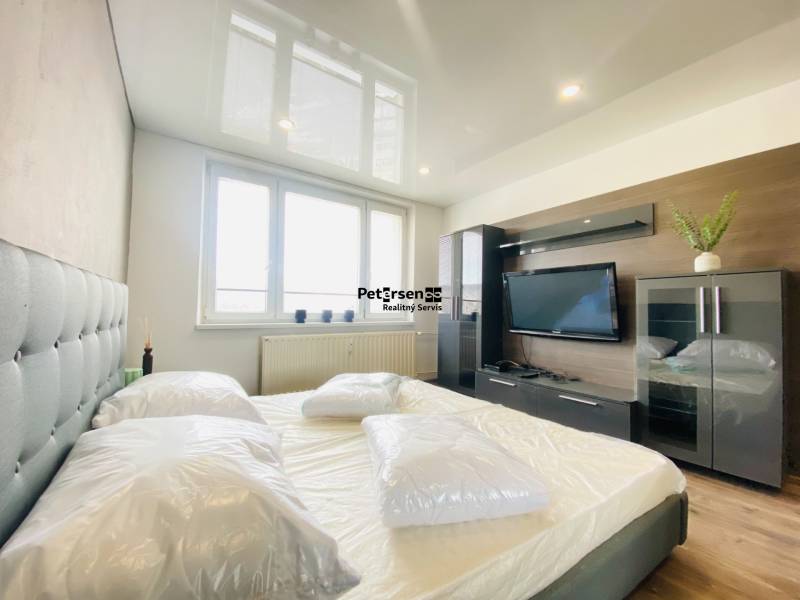 A bedroom in a 3-room apartment with an upholstered bed, a television, and a wooden decor floor.