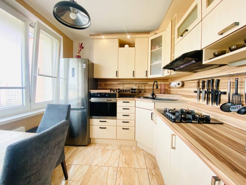 A kitchen in a 3-room apartment furnished with light-colored furniture and a dining table.