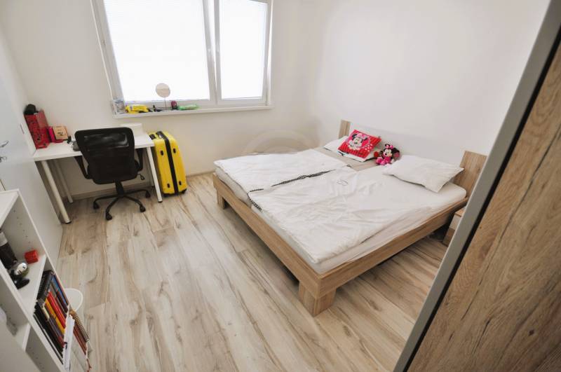 Bright bedroom in a 2-room apartment with a bed, a desk, and a floor with a wooden decor.
