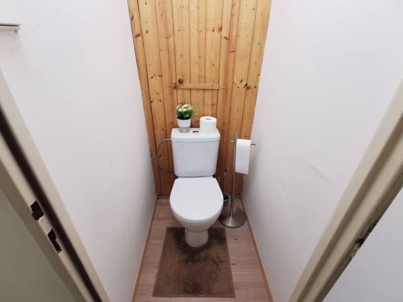 A toilet with a toilet bowl, wooden paneling, and a floor with a wooden decor in a 2-room apartment.