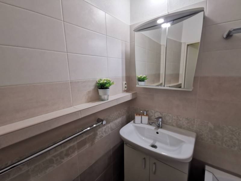 Bathroom in a 2-room apartment with a sink, mirror, and tiles in neutral shades.