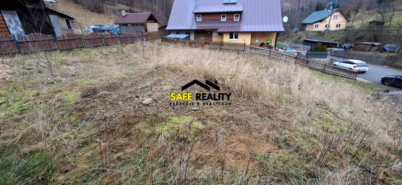 A plot of land for residential use in Oščadnica with a sloping terrain and neighboring houses in the background.