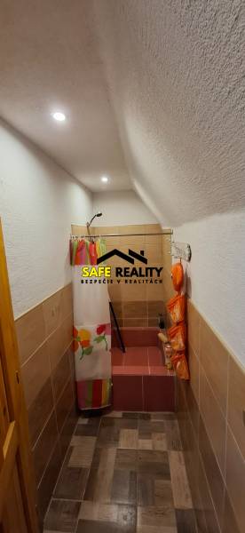 A house with a narrow bathroom, a colorful shower curtain, and a floor with a wooden decor.