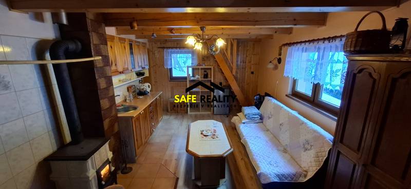 Interior of a cabin with wooden elements, a kitchen, a sofa, and a stove.