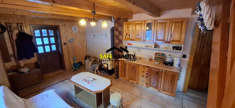 Interior of a cabin with wooden decor, kitchen unit, wood-burning stove, seating area.