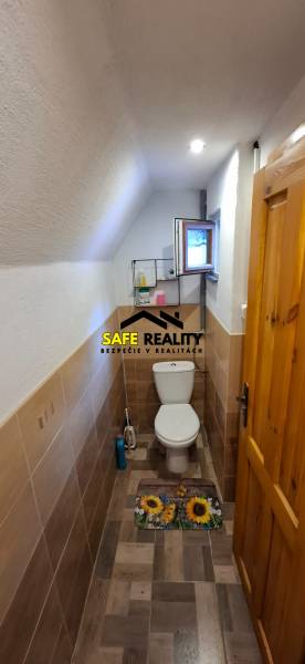 Toilet in a cabin with a wooden decor floor, storage shelves above the toilet.