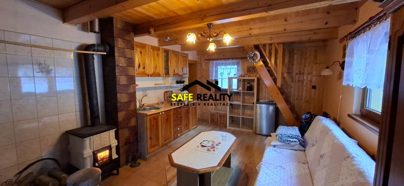 A wooden interior of a cabin with a fireplace, kitchen, and floor with wooden decor.