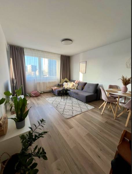 Living room in a two-room apartment with a sofa, table, and wooden decor flooring.