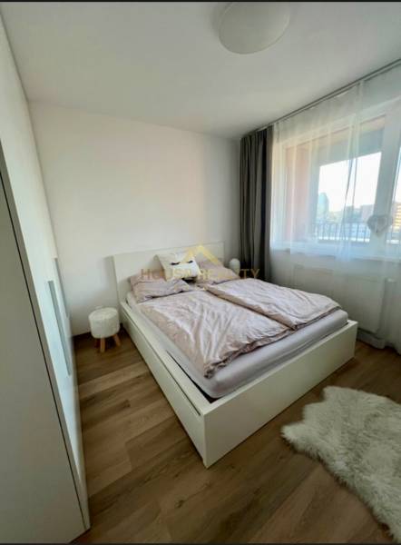 A bedroom with light furnishings, wood-patterned flooring, and a window in a 2-room apartment.