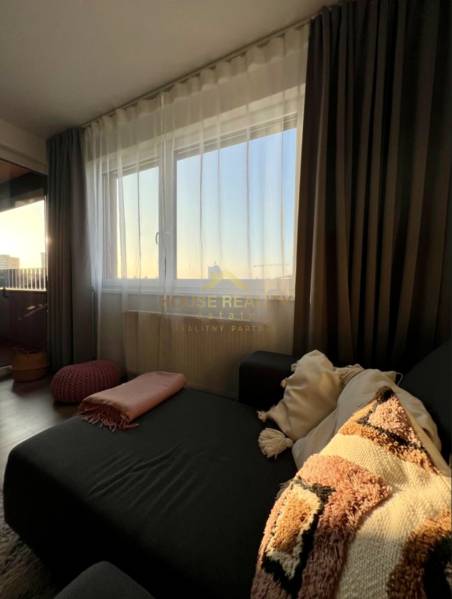 Living room of a two-room apartment with a sofa, cushions, and curtains.